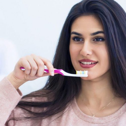 Collins-St-Dental-Arlington-TX-Woman-brushing-teeth-with-dentists-in-background-min-scaled-ojsbday9ikorxadxeip4u94s8vr9lgyisj9hgdy7pk